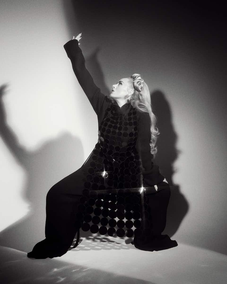 Adele wearing a black dress, trousers and jumper which are all Marc Jacobs. The photo is in black and white, shot by Charlotte Wales for The Face magazine.