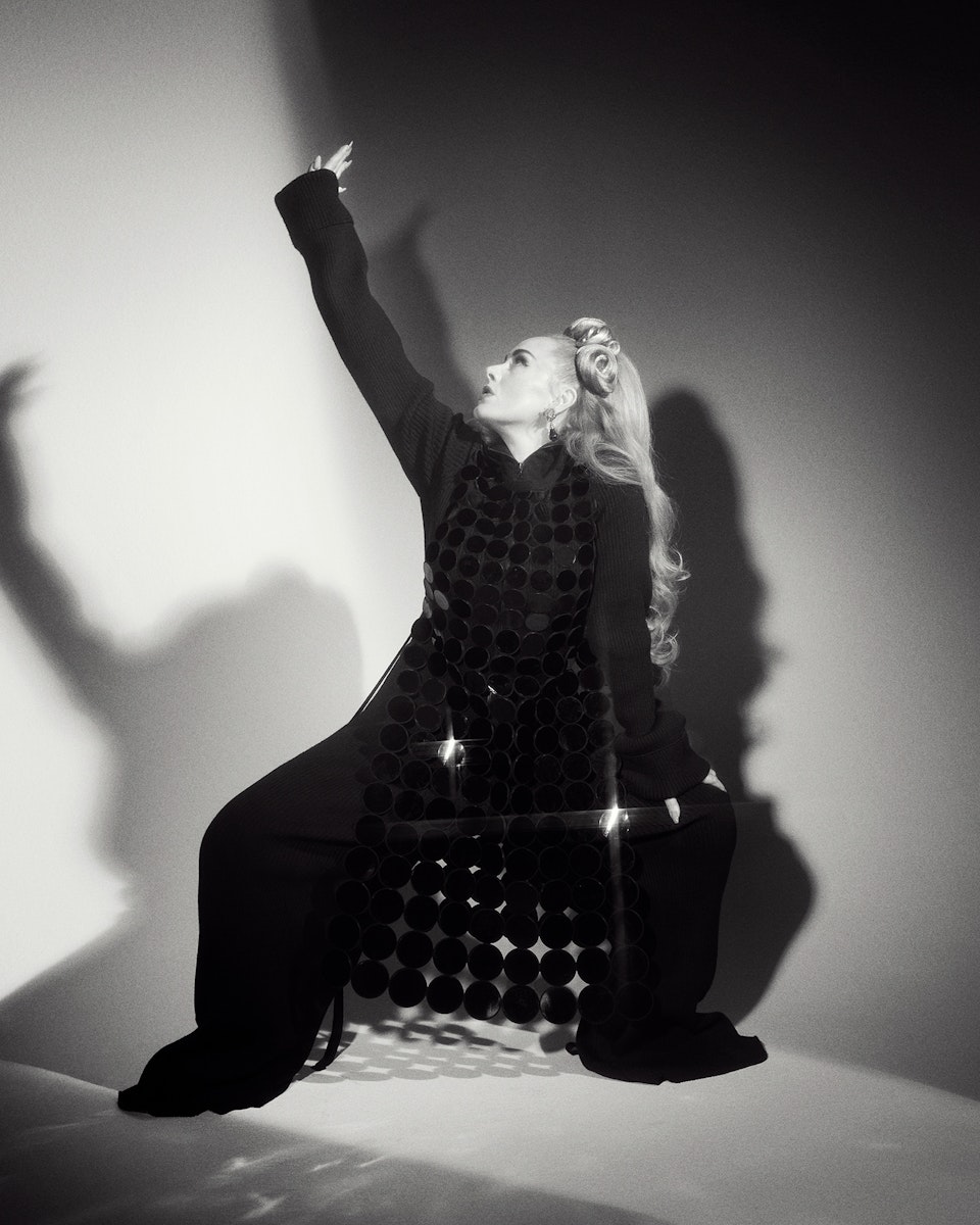 Adele wearing a black dress, trousers and jumper which are all Marc Jacobs. The photo is in black and white, shot by Charlotte Wales for The Face magazine.
